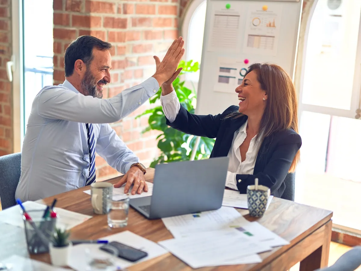 An HR manager and a new hire reviewing onboarding paperwork together at an office desk with a laptop